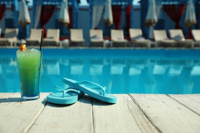 Photo of Refreshing cocktail and flip flops near swimming pool on sunny day. Space for text