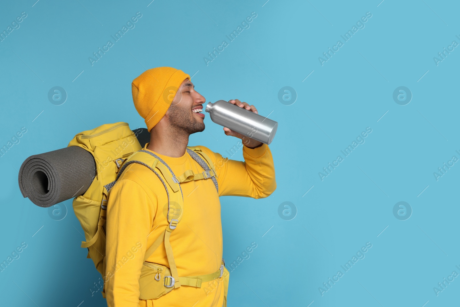 Photo of Happy tourist with backpack drinking on light blue background, space for text