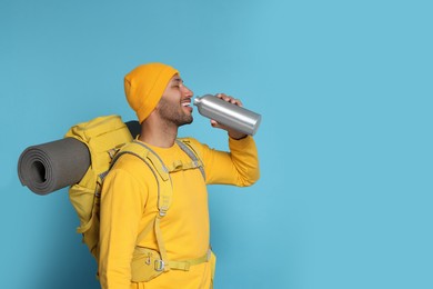 Happy tourist with backpack drinking on light blue background, space for text