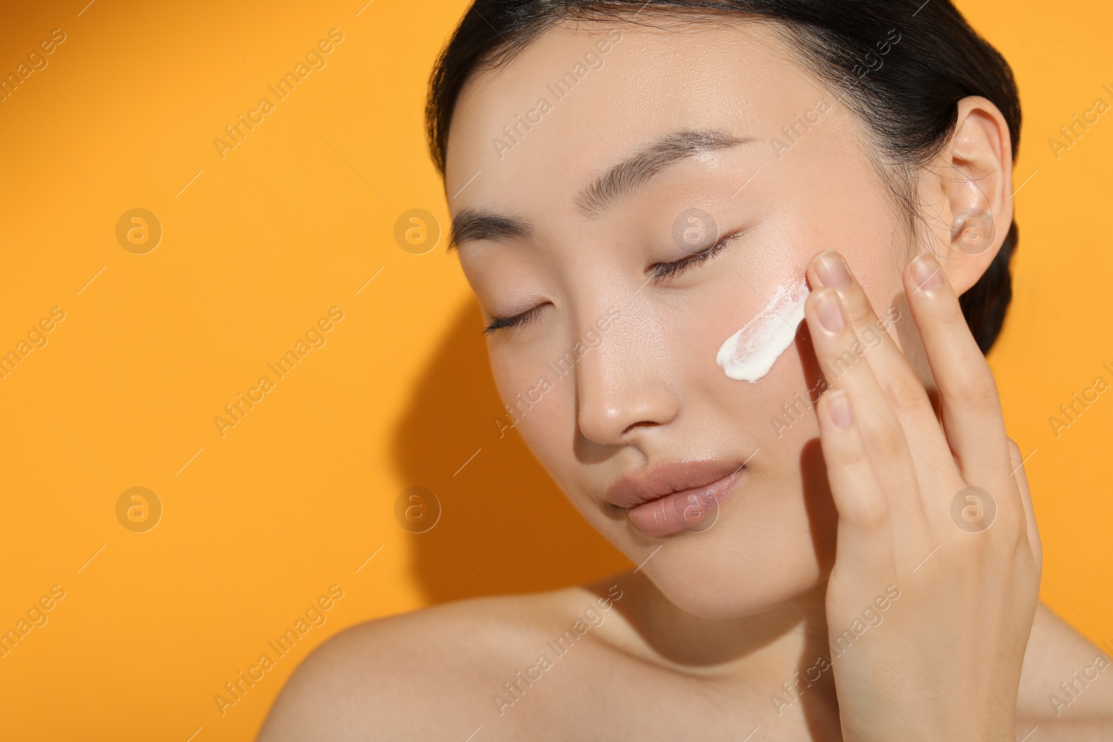 Photo of Beautiful young woman in sunlight with sun protection cream on her face against orange background, closeup. Space for text