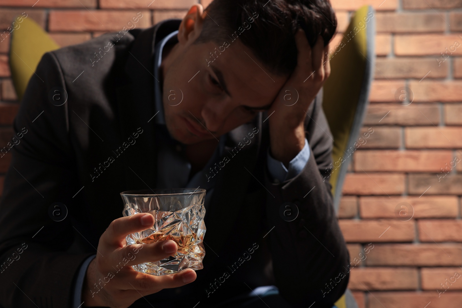 Photo of Addicted man near red brick wall, focus on glass of alcoholic drink