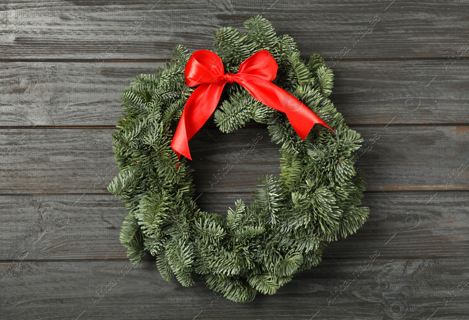 Photo of Christmas wreath made of fir tree branches with red ribbon on black wooden background