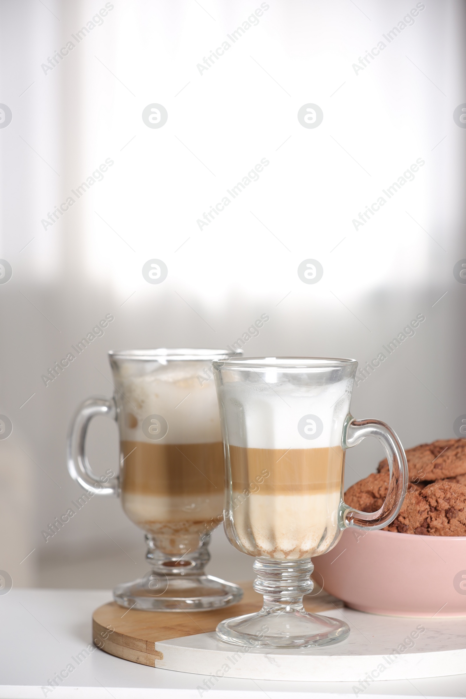 Photo of Aromatic latte macchiato in glasses and chocolate cookies on white table against light background