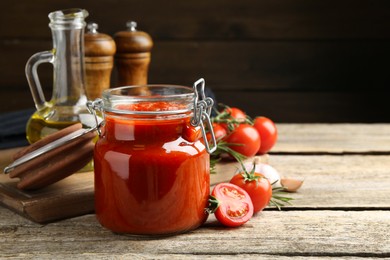 Photo of Homemade tomato sauce in jar and ingredients on wooden table, closeup. Space for text