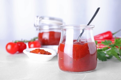 Jar of hot chili sauce with spoon and ingredients on table. Space for text