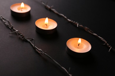 Photo of Burning candles and barbed wire on black background. Holocaust memory day