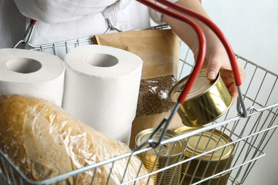 Photo of Woman holding shopping basket with products and toilet paper rolls, closeup. Panic caused by virus