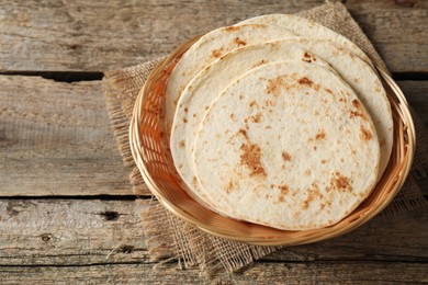 Photo of Tasty homemade tortillas in wicker basket on wooden table, space for text