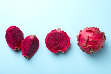 Photo of Delicious cut and whole red pitahaya fruits on light blue background, flat lay