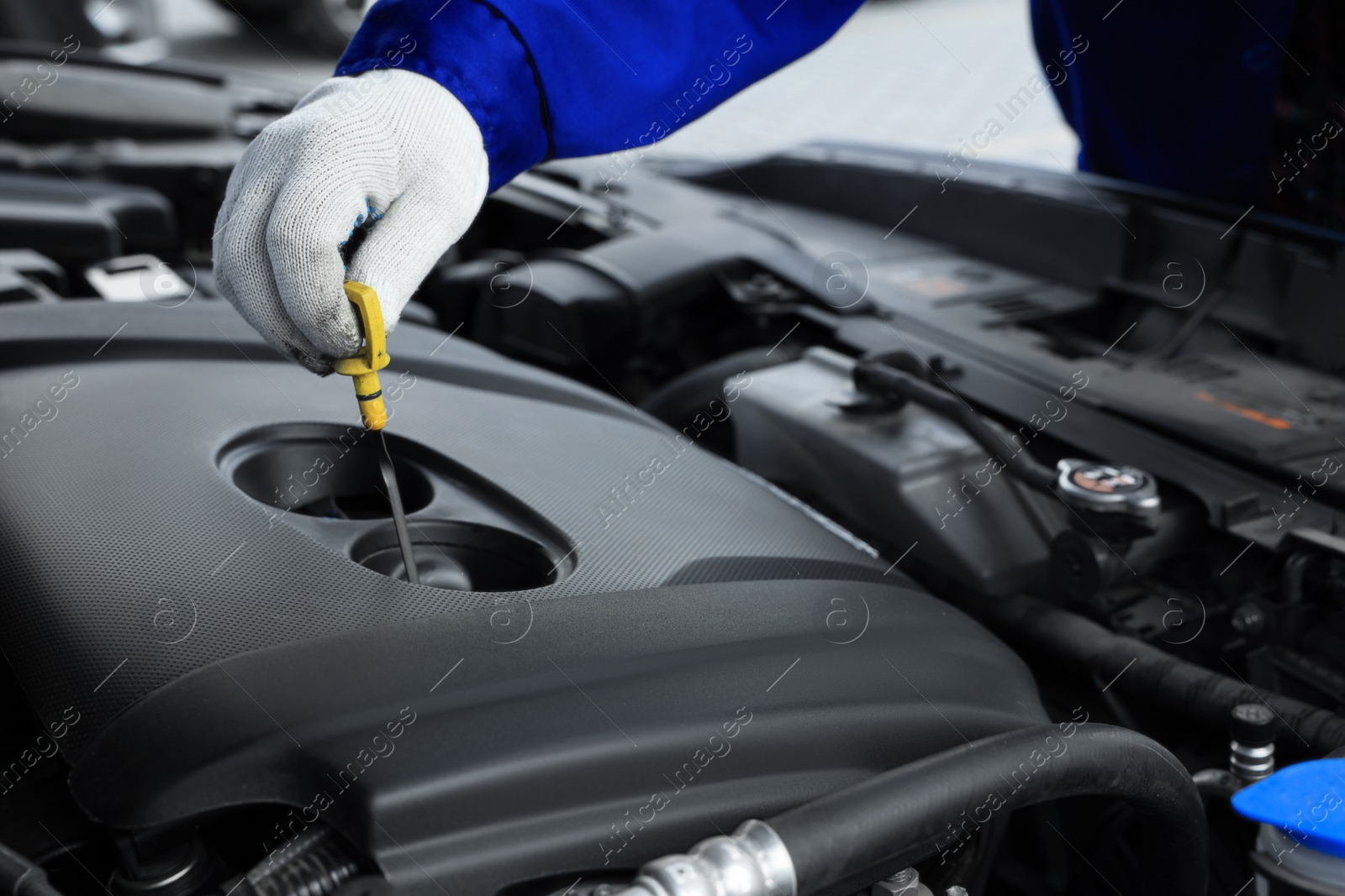 Photo of Worker checking motor oil level in car with dipstick, closeup