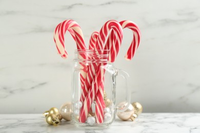 Photo of Candy canes in mason jar and Christmas balls on white marble table