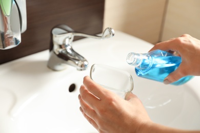 Woman pouring mouthwash from bottle into glass in bathroom, closeup. Teeth care