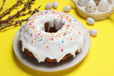 Photo of Easter cake with sprinkles, painted eggs and willow branches on yellow background