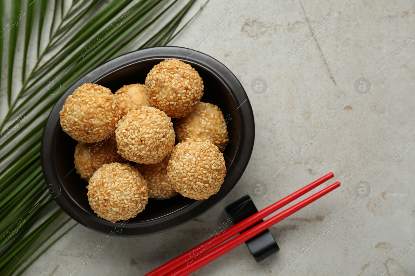 Photo of Delicious sesame balls, green leaf and chopsticks on textured table, flat lay. Space for text