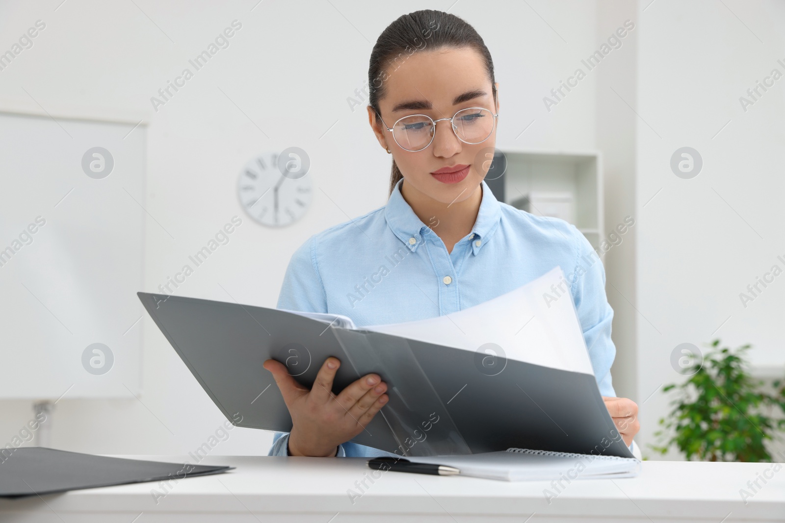 Photo of Young female intern with folder working at table in office