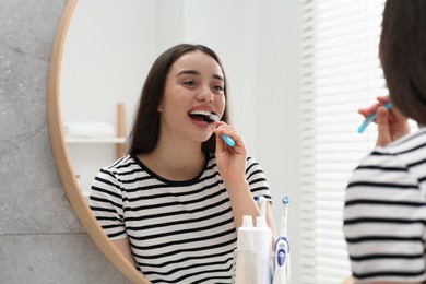 Photo of Young woman brushing her teeth with plastic toothbrush near mirror in bathroom