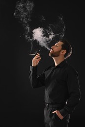 Man using cigarette holder for smoking on black background, space for text