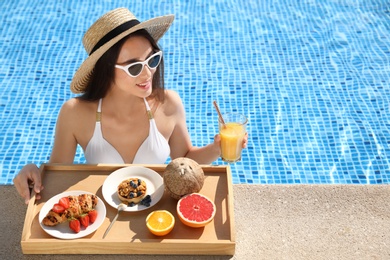 Young woman with delicious breakfast on tray in swimming pool. Space for text