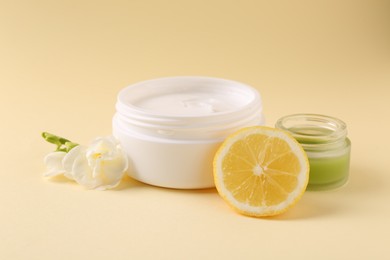 Moisturizing cream in open jars, lemon and freesia flower on beige background. Body care products