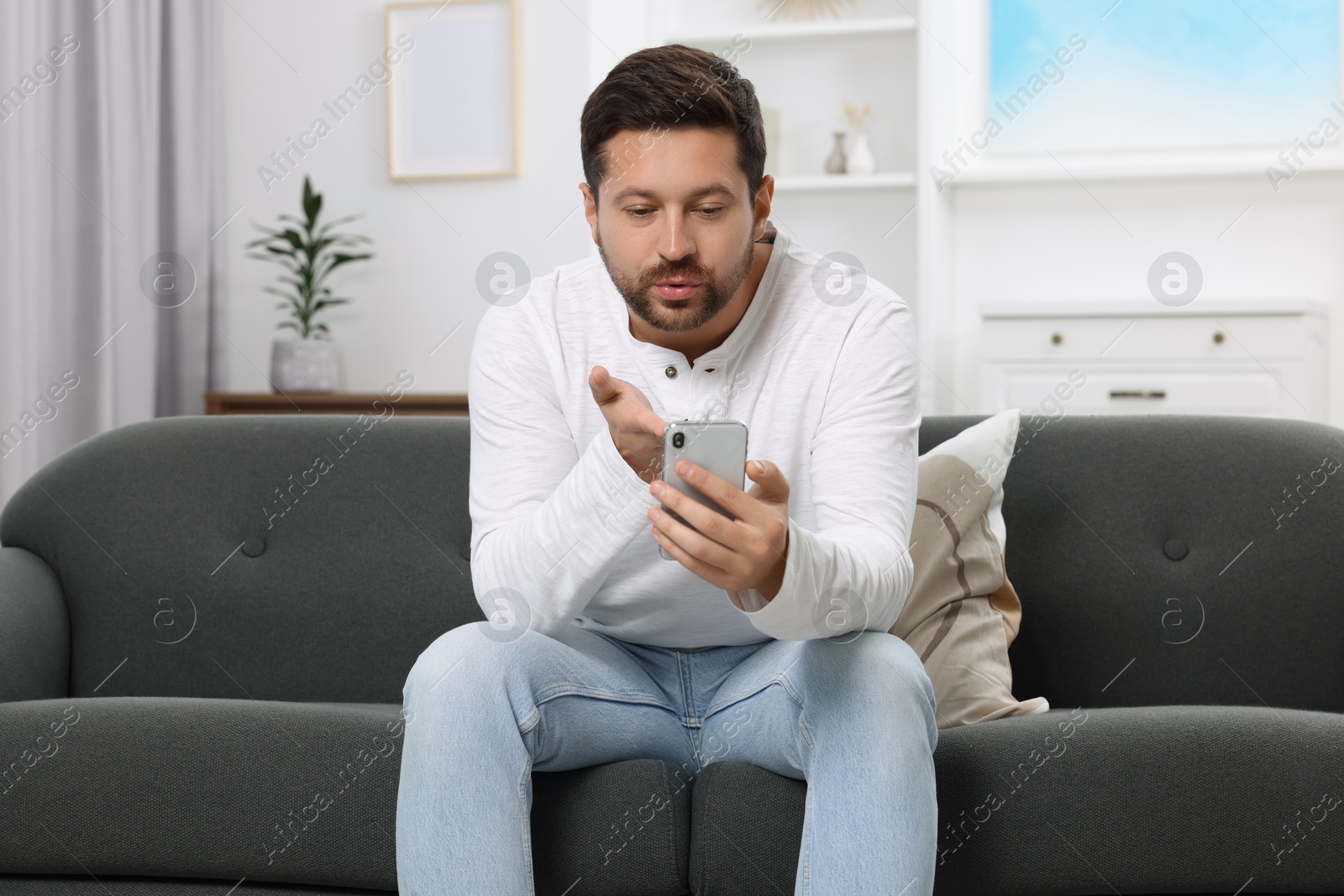 Photo of Man blowing kiss during video chat via smartphone at home. Long-distance relationship