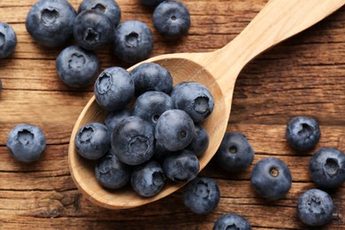 Photo of Spoon with tasty fresh blueberries on wooden table, flat lay