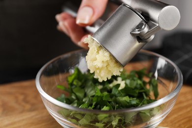 Woman squeezing garlic with press at wooden table, closeup