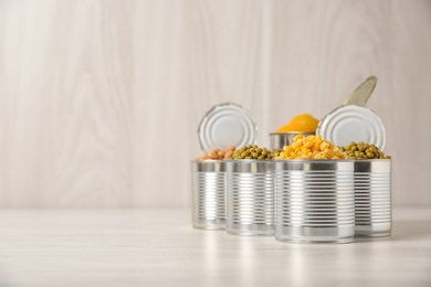 Photo of Open tin cans with conserved vegetables and fruits on light table. Space for text