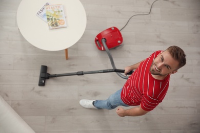 Young man using vacuum cleaner at home, top view