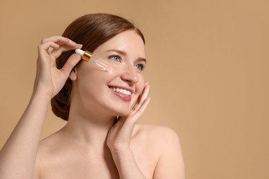 Photo of Smiling woman with freckles applying cosmetic serum onto her face on beige background. Space for text