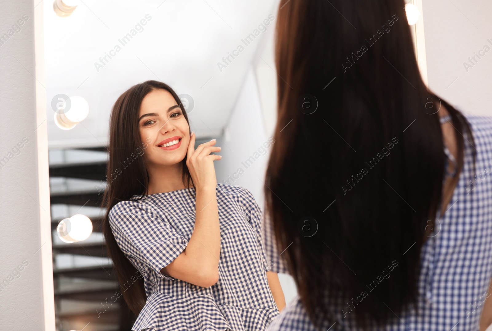 Photo of Young attractive woman looking at herself in stylish mirror at home