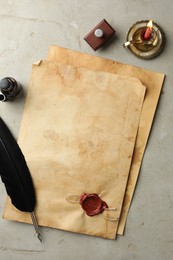 Photo of Sheet of old parchment paper with wax stamp, black feather, inkwell and candle on grey table, flat lay