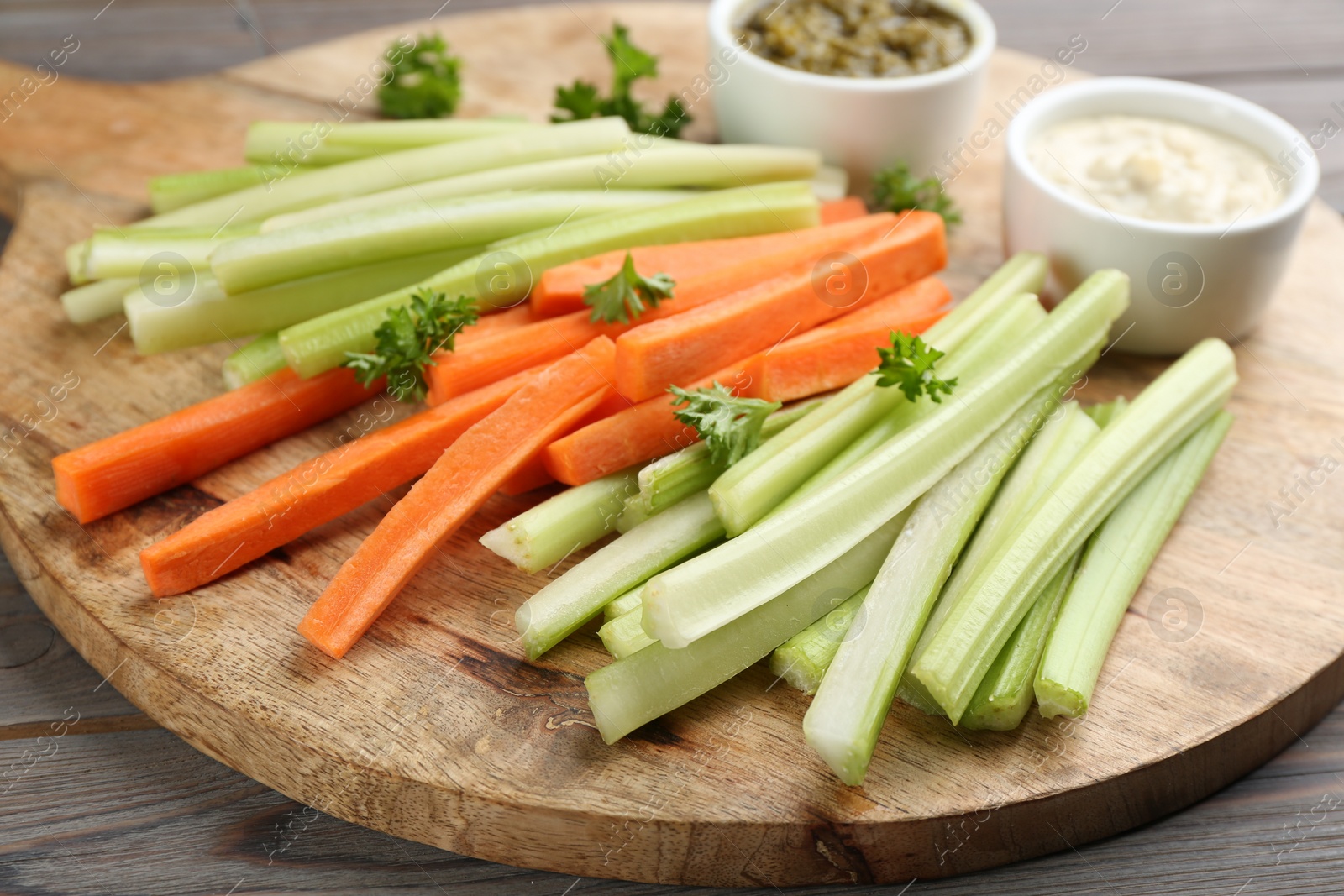 Photo of Celery and other vegetable sticks with different sauces on wooden board
