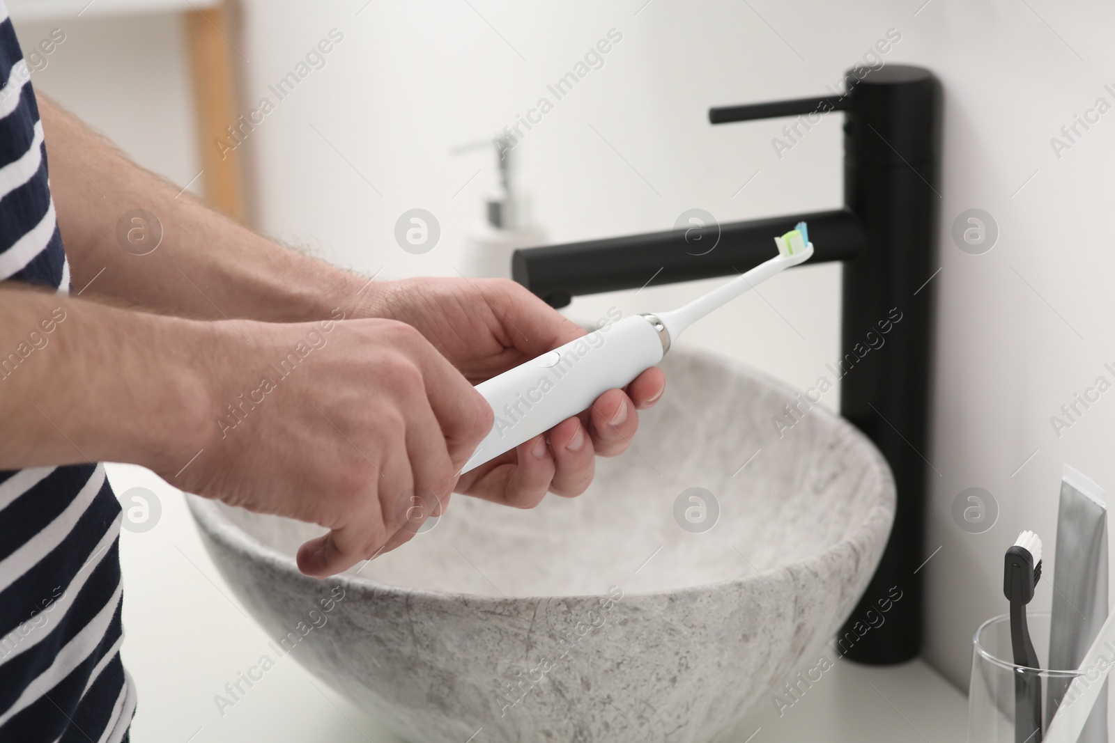 Photo of Man holding electric toothbrush above sink in bathroom, closeup