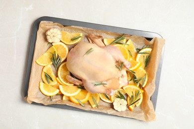Photo of Chicken with orange, rosemary and garlic in baking tray on light table, top view