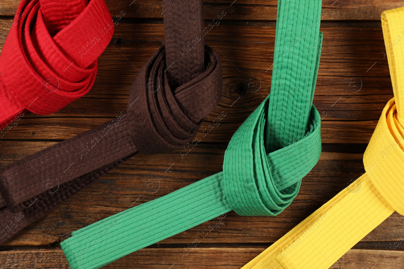 Photo of Colorful karate belts on wooden background, flat lay