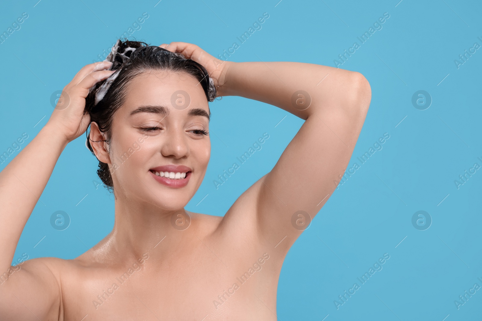 Photo of Beautiful happy woman washing hair on light blue background. Space for text