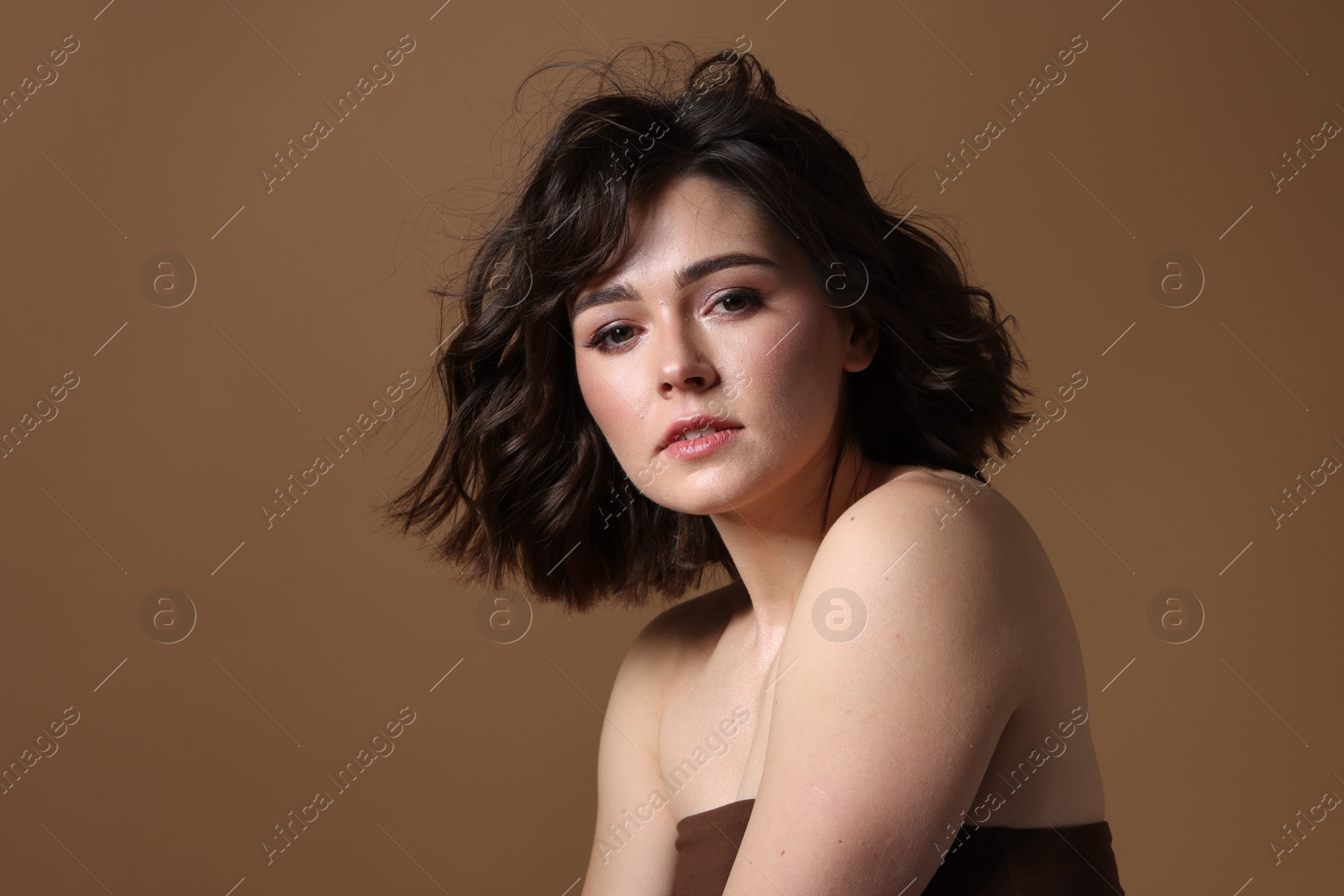 Photo of Portrait of beautiful young woman with wavy hairstyle on brown background. Space for text