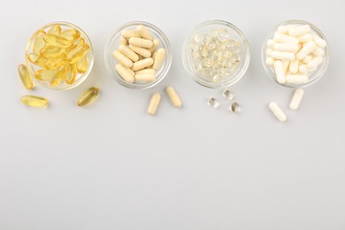 Photo of Glass bowls with different vitamin capsules on light grey background, flat lay. Space for text
