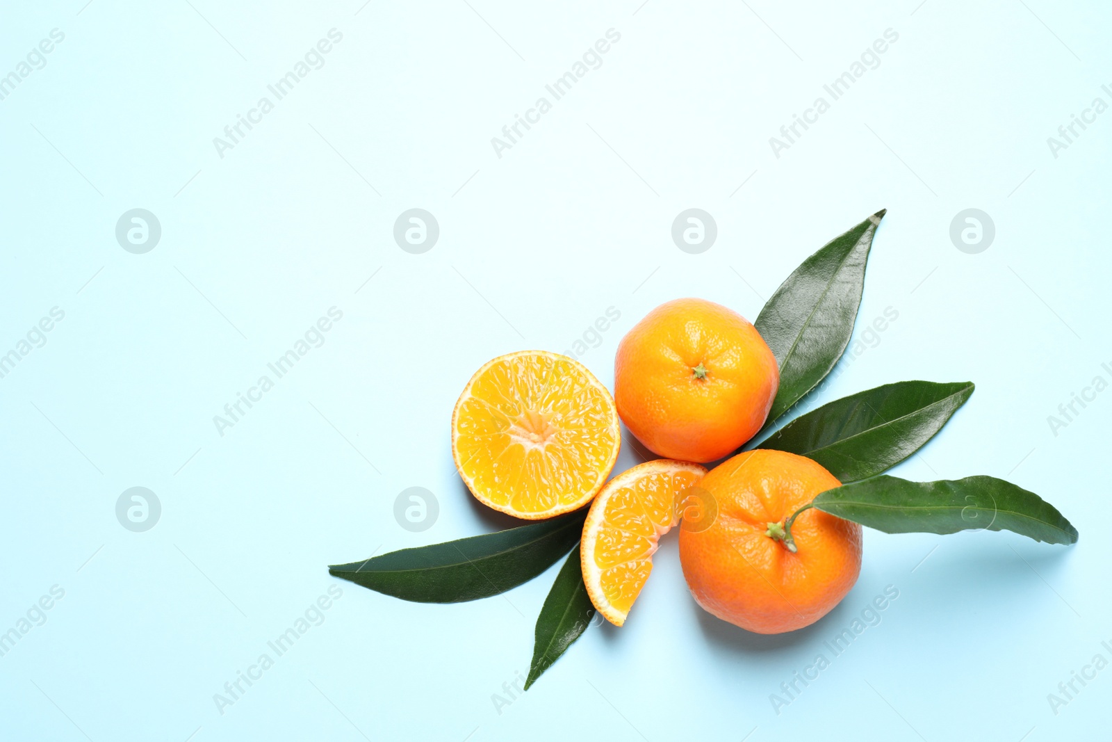 Photo of Flat lay composition with fresh ripe tangerines and leaves on light blue background, space for text. Citrus fruit