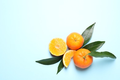 Flat lay composition with fresh ripe tangerines and leaves on light blue background, space for text. Citrus fruit