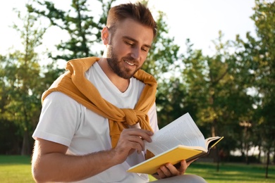 Photo of Young man reading book in park on sunny day