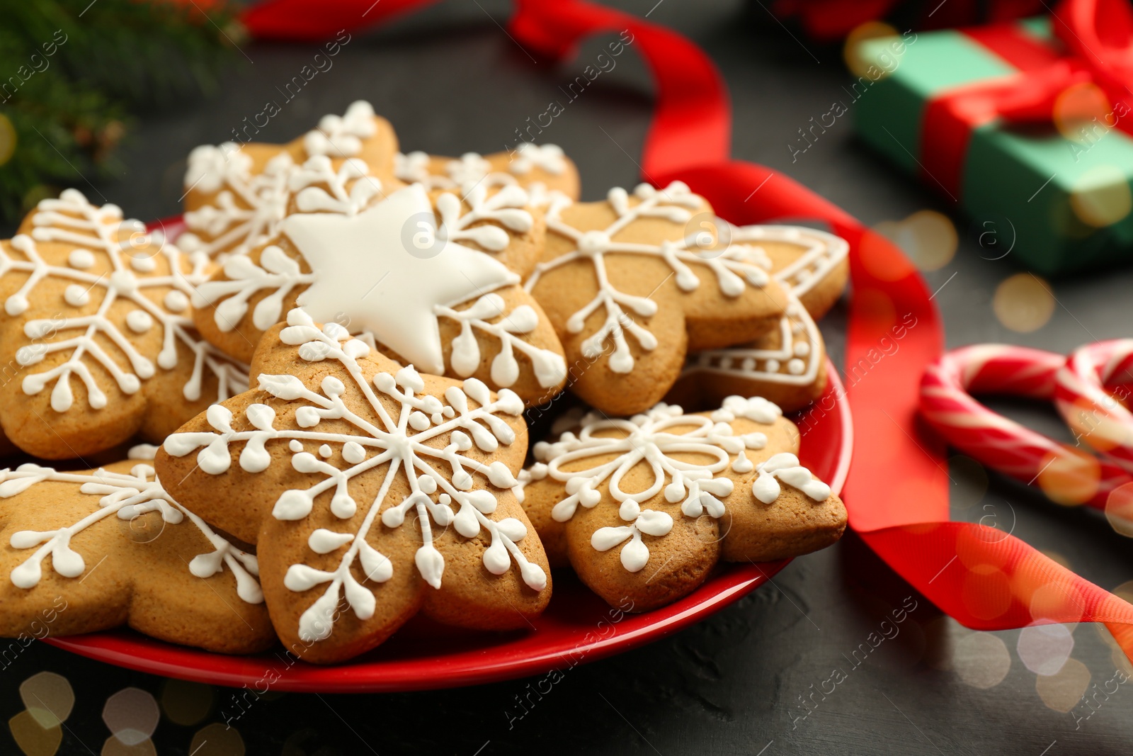 Photo of Tasty Christmas cookies with icing and red ribbon on black table, closeup