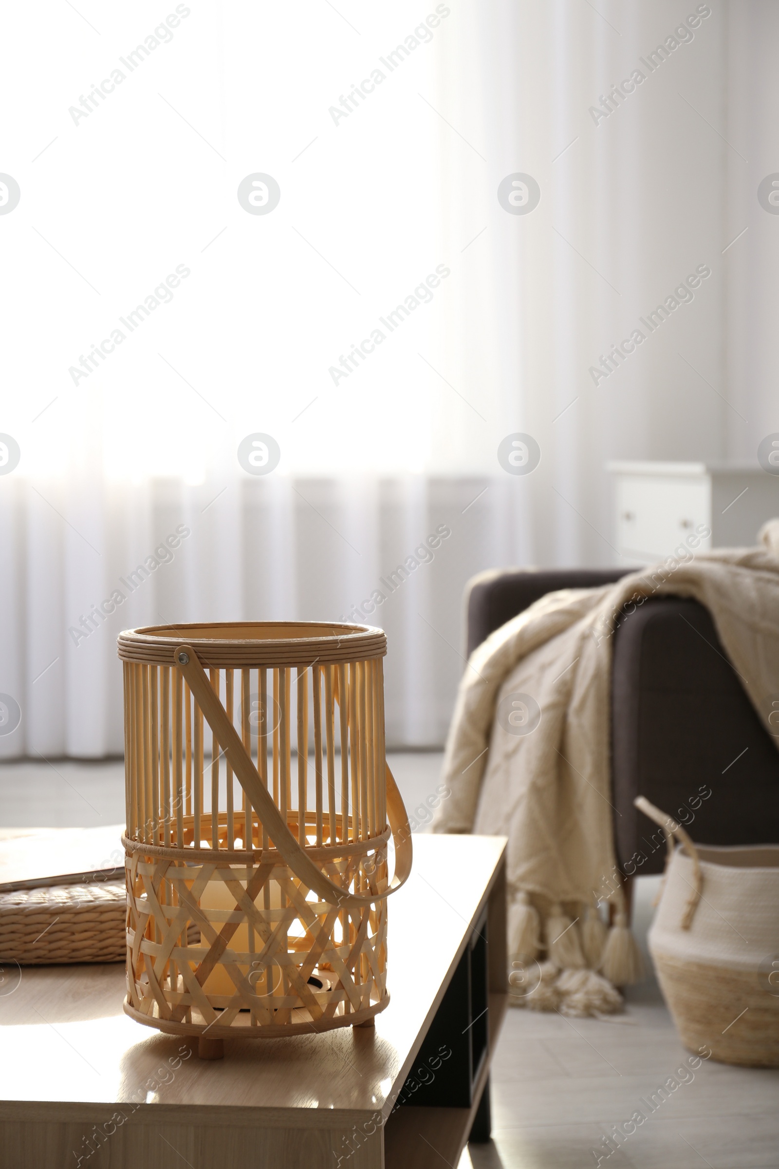 Photo of Stylish wicker holder with candle on wooden table indoors, space for text