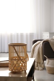 Photo of Stylish wicker holder with candle on wooden table indoors, space for text