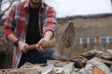 Photo of Man breaking bricks with sledgehammer outdoors, selective focus