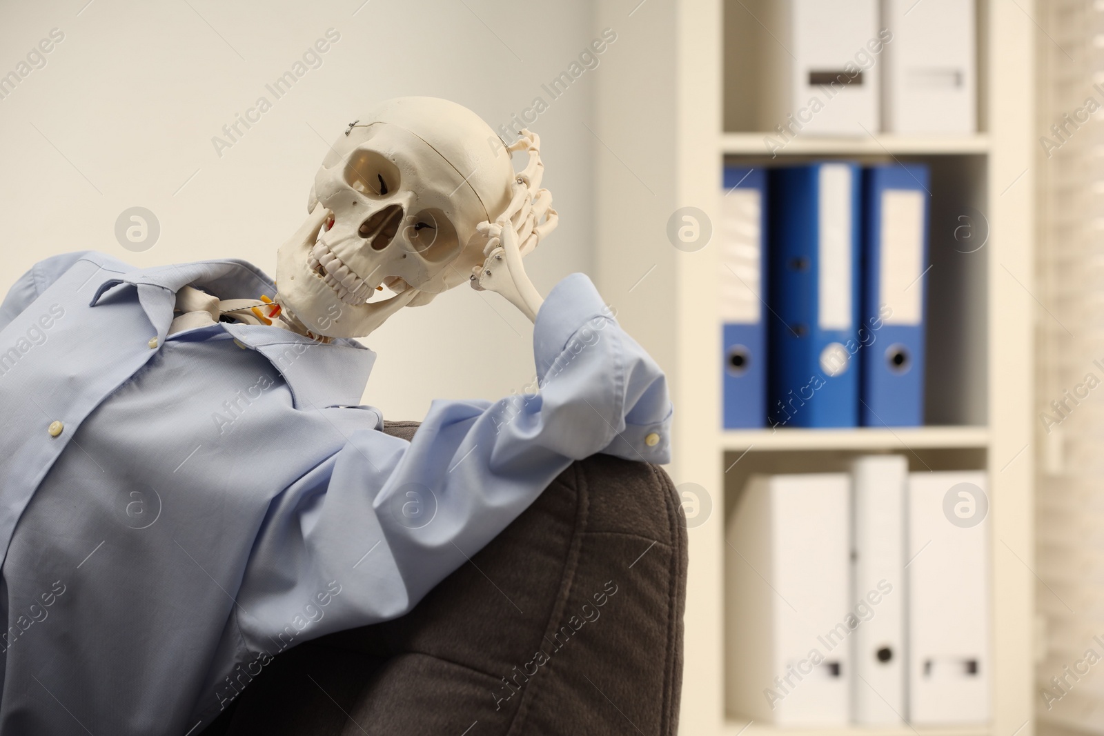 Photo of Waiting concept. Human skeleton sitting in armchair at office