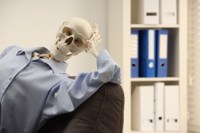 Waiting concept. Human skeleton sitting in armchair at office