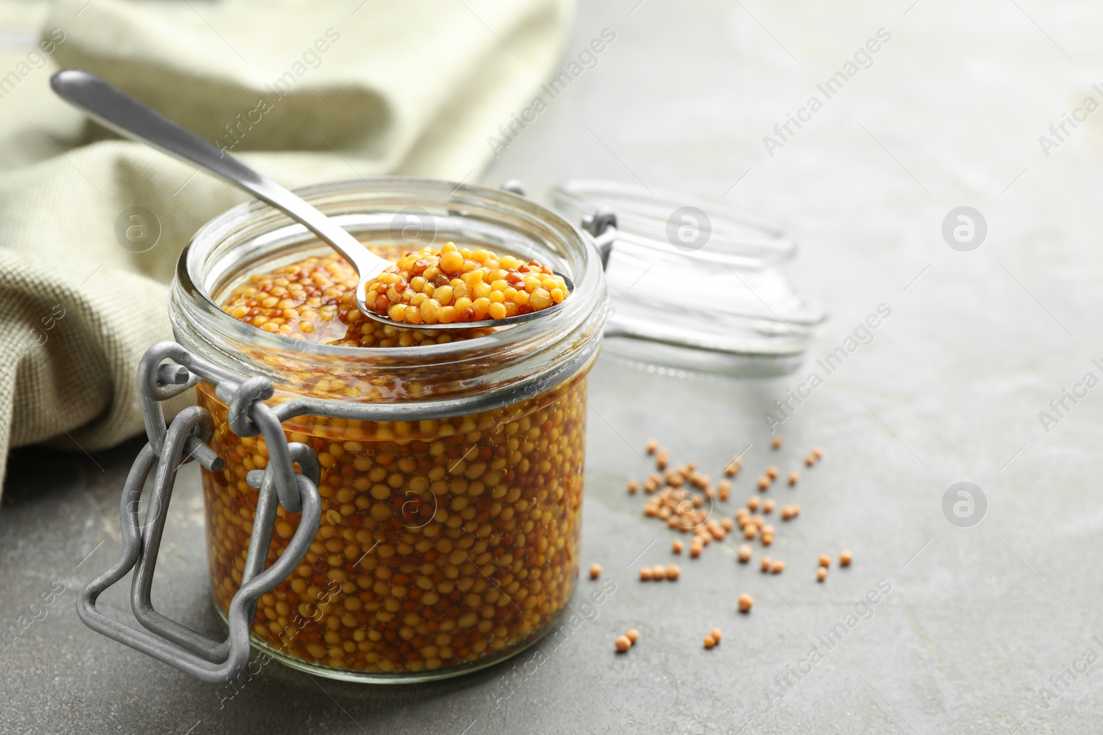 Photo of Whole grain mustard in jar and spoon on grey table. Space for text