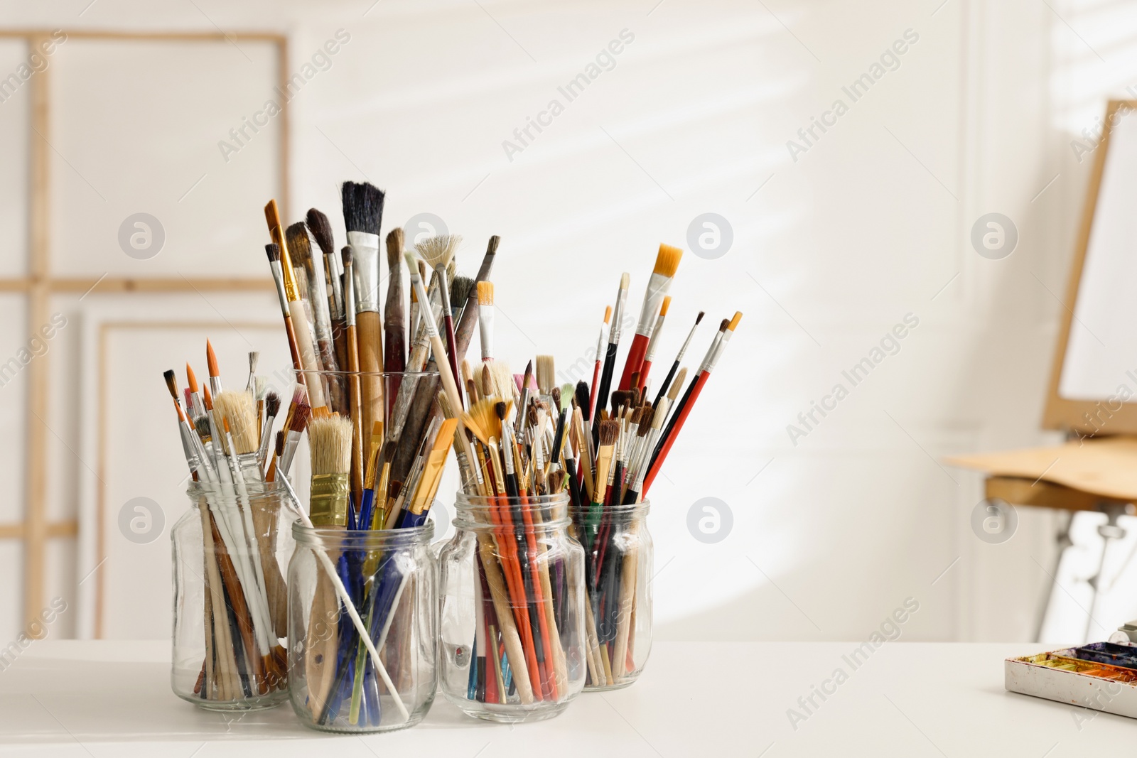 Photo of Different paintbrushes on white table in studio, space for text. Artist's workplace