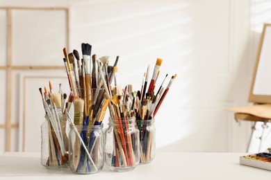 Photo of Different paintbrushes on white table in studio, space for text. Artist's workplace
